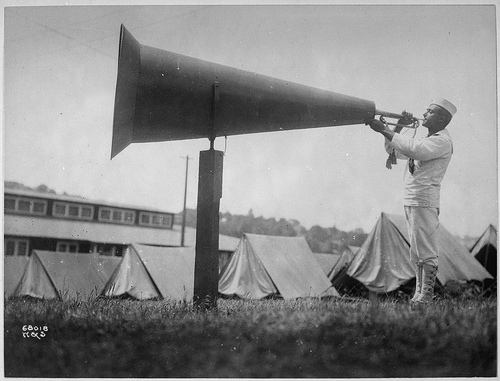 black and white photograph of a person in a military uniform playing a bugle into a large megaphone